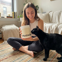 Woman holding a tub of Meowie with her black cat