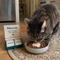 Senior cat eating beside the Meowie Senior Omega-3 box